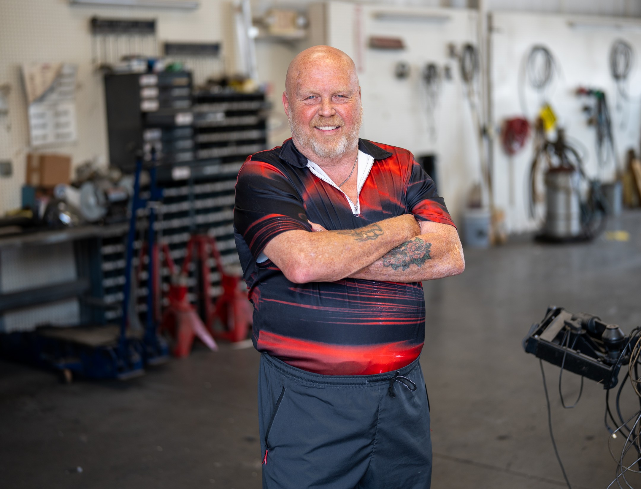 man smiling at camerain black and red shirt, inside truck repair shop